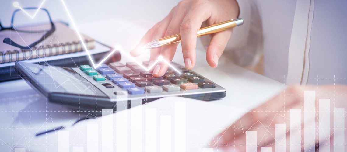 Accountant calculating profit with financial analysis graphs. Notebook, glasses and calculator lying on desk. Accountancy concept. Cropped view.